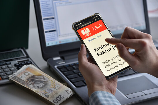 Wroclaw, Polska - 24 stycznia 2026: Od 1 lutego obowiazkowy system KSeF, rejestracja faktur online. Na zdjeciu: telefon ze strona KSEF, gotowka, kalkulator i laptop w tle.