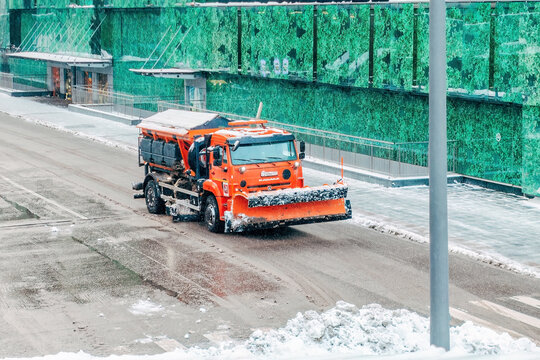 orange road maintenance vehicle (a combined road machine) equipped for winter conditions, parked on a wet, icy road