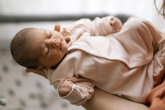 Newborn baby sleeping peacefully in soft pink outfit while being held gently