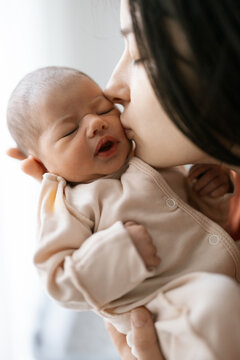 Mother gently kisses newborn baby&rsquo;s cheek in soft, quiet moment of love and care