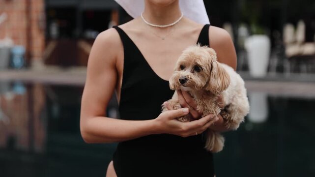 Woman enjoying a luxurious vacation, holding a beloved small pet dog poolside at a high-end travel destination