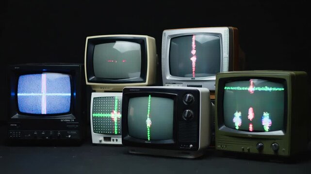 Retro cathode-ray tube monitors stacked in dark room. Multiple screens showing distorted crosshair graphics and electronic interference.