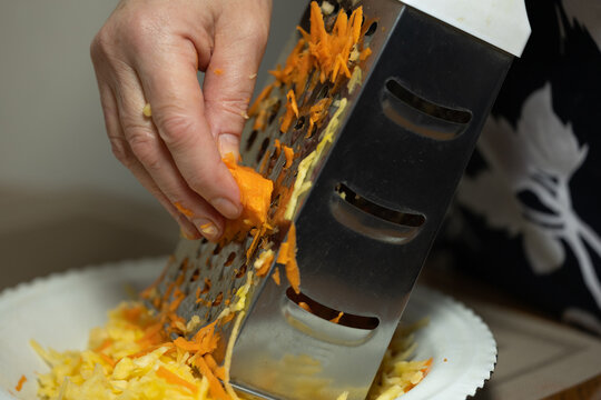 A chef hand-grates carrots for a salad.