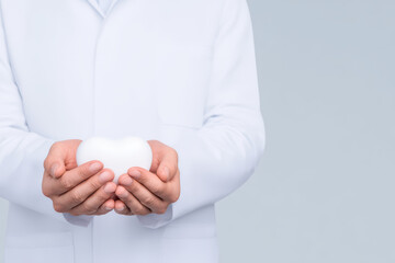 White heart shape held by medical professional hands in white coat, symbolizing care, health, and compassion in clean, minimal style close up image