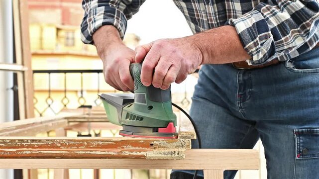 Craftsman. Adult carpenter using an electric sander to smooth an old wooden window. Construction industry, carpentry, housework do it yourself. Restoration. Footage.