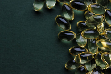Top view of omega-3 fish oil capsules scattered on a dark green background with copy space.