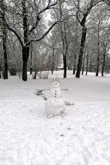 A humorous snowman in a quiet winter park during a cloudy day, with snow-covered trees in the...
