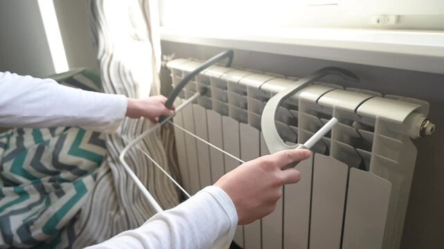 Hands attach a portable clothes drying rack to a home radiator, utilizing it for efficient indoor laundry drying, especially in colder months.