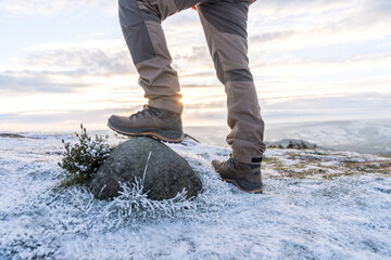 Hiker steps on a rock during sunrise on a frosty mountain trail in winter