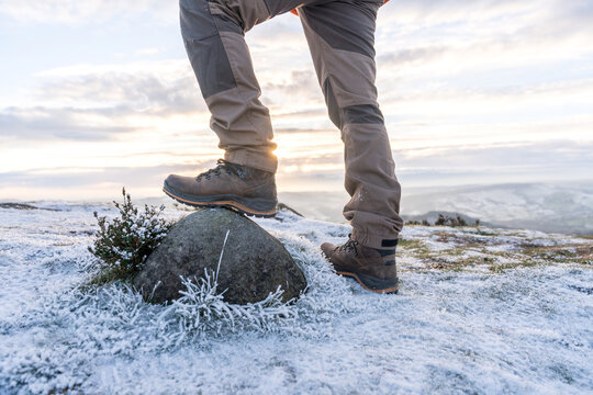 Hiker steps on a rock during sunrise on a frosty mountain trail in winter