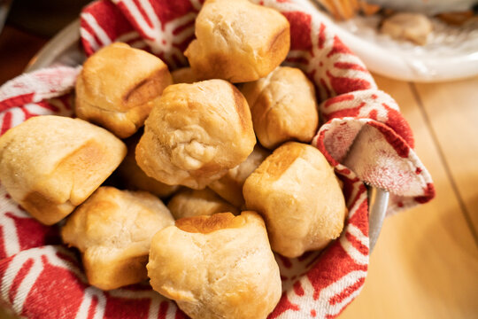 basket filled with freshly baked golden brown dinner rolls, wrapped in a red and white cloth napkin and placed on a wooden table