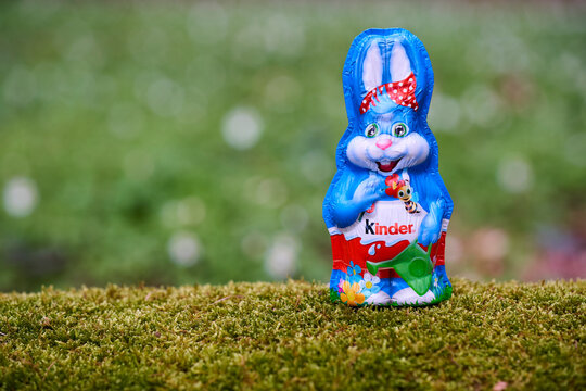Kinder chocolate bunny on outdoor rock, festive foil wrap with bee and flower, springtime nature background.