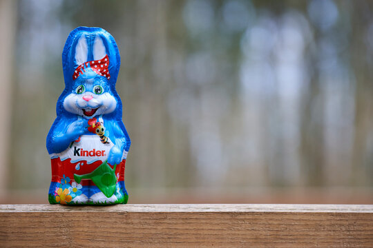 Kinder chocolate bunny on wooden surface with forest background, festive foil design and spring-themed illustrations.