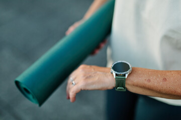 Obraz premium Portrait of a mid age mature sport woman smiling happy and confident, prepering for jogging and run looking at her watch and performance. Running in city park outdoors