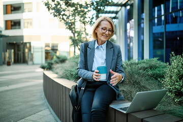 Portrait of a middle aged mature businesswoman woman using a laptop computer and holding a cup of...