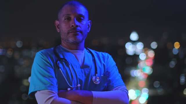 Serious male doctor or paramedic standing with arms crossed at night with flashing emergency lights