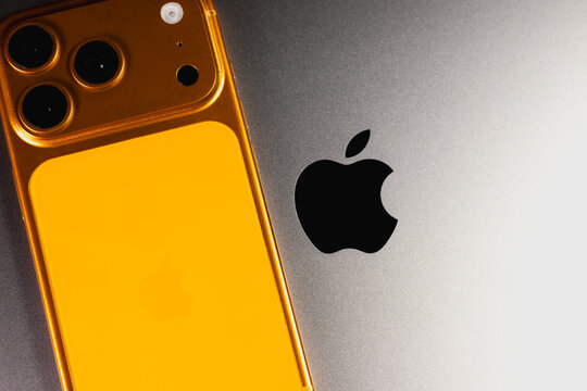 KYIV, UKRAINE - January 22, 2026 : Apple iPhone 17 Pro in Cosmic Orange color lie on gray Macbook Pro laptop. Apple company logo, close up.