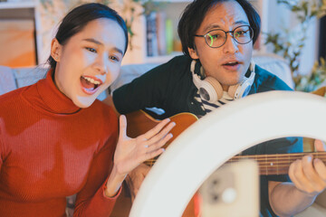 alented Asian musician and singer host a live stream concert from home at night, using a ring light for a professional online broadcast and influencer experience