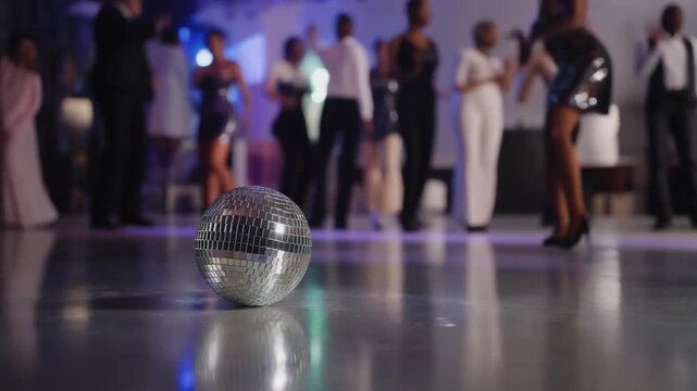 A disco ball sits on a reflective dance floor at a formal event. Blurred figures of elegantl.