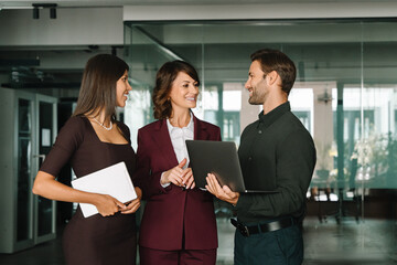 Teamwork, communication, networking corporate culture office environment. Successful professional smiling colleagues, business partners holding laptop talking during collaborative working discussion
