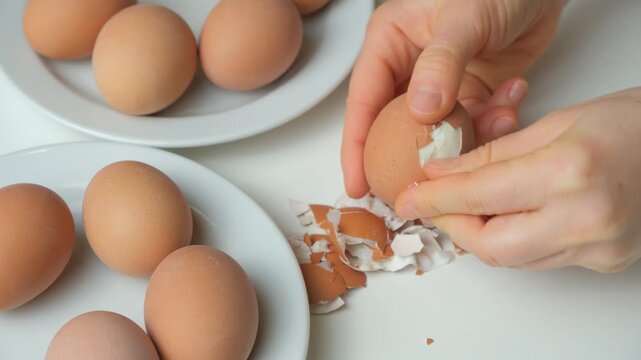 Close up of hands peeling the shell off a hard boiled egg.