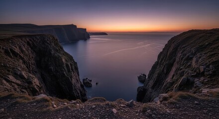 Fototapeta premium Coastal cliffs meet calm sea at dusk, rocks below, soft light on the horizon