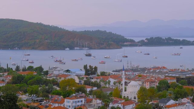 Time lapse: sailing yachts and small boats anchored in calm Fethiye Bay. Boats are sailing fast. View of residential buildings. Timelapse, seascape, travel, and coastal lifestyle concept