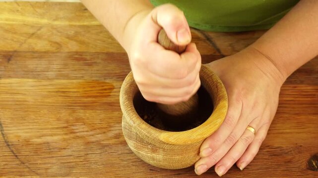 Woman grinding spices for meat in a wooden mortar