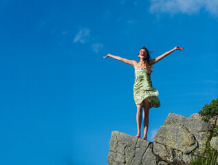 Obraz premium Woman enjoying freedom on mountain rock under blue sky. Carefree girl standing with open arms. Carefree summer. Carefree female feeling happiness on fresh air. Carefree young woman outdoors.