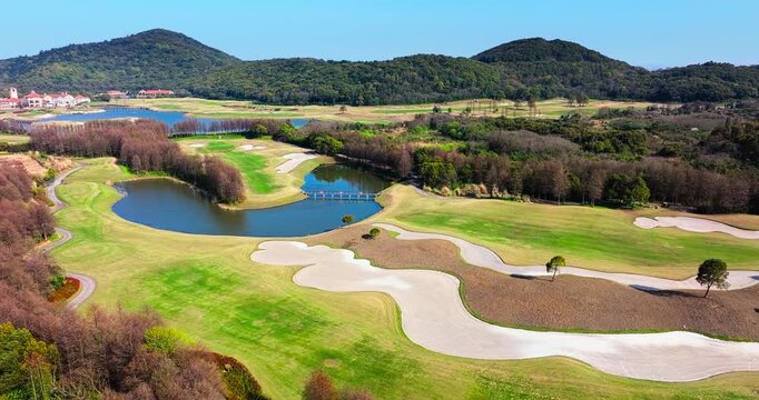 Scenic aerial view of a luxury golf course stretching across the landscape with green fairways and a blue lake under a clear sunny sky.
