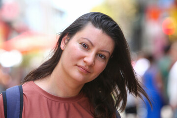 Obraz premium Close-up portrait of an adult woman with backpack smiling and looking at the camera on a busy city street.