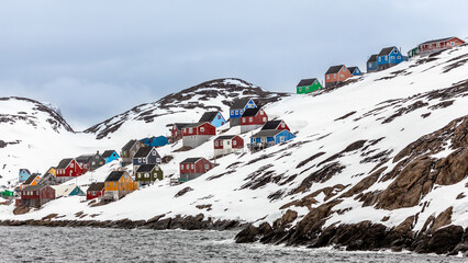 Traditional village with brightly painted houses built on snow covered rocky slopes by the sea, illustrating isolation and arctic coastal landscape, Kangamiut, Greenland © vadim.nefedov
