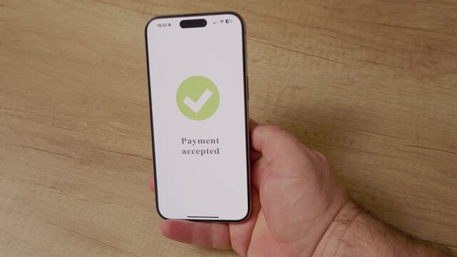 A man holds a smartphone displaying a payment accepted message. The action shows the process of making a purchase using mobile payment technology.