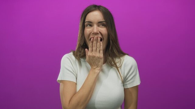 Woman covers mouth with finger to lips in pink studio setting demonstrating silence gesture; secret surprise.