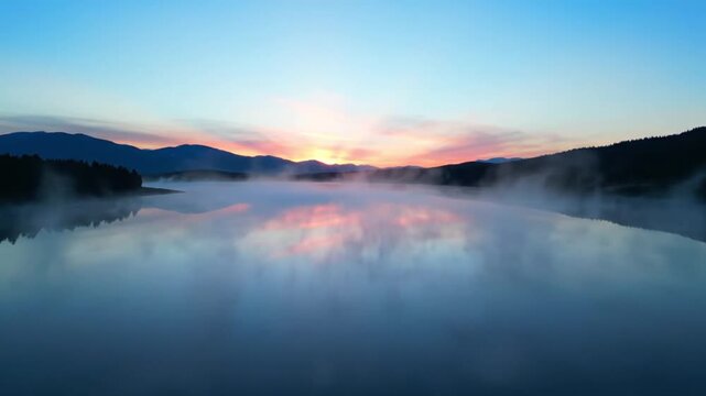 Misty lake at sunrise reflecting colorful sky and mountain silhouettes, peaceful morning landscape with copy
