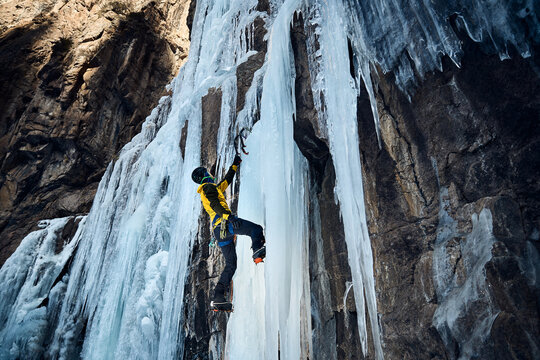 Man climbing frozen ice wall at winter mountains