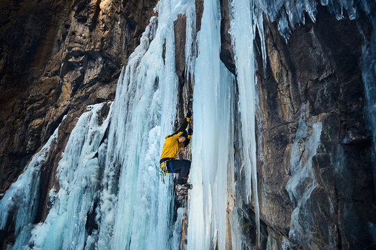 Man climbing frozen ice wall at winter mountains
