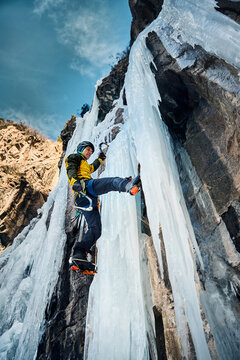 Man climbing frozen ice wall at winter mountains