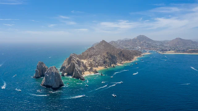 Panoramic aerial view of Land’s End at the southern tip of the Baja California Peninsula in Cabo San Lucas, Mexico. The shot reveals the iconic rock formations, turquoise waters of the Sea of Cortez.