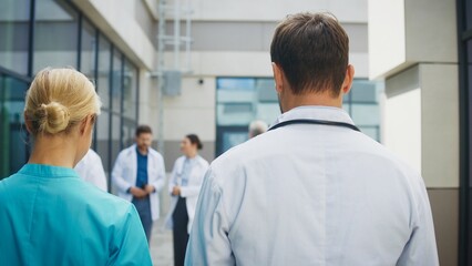 Obraz premium Smiling female nurse walking beside focused male doctor outside clinic. Confident pair discussing duties while moving along pathway. Professional team sharing thoughts during relaxed moment.