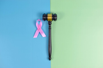 Judge gavel and pink ribbon on split blue-green background, symbolizing justice and breast cancer awareness through contrasting visual elements.