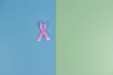 Pink ribbon on blue-green background, symbolizing breast cancer awareness through simple composition and strong color contrast.