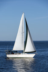 Sailboat with white sails on calm blue sea under clear sky