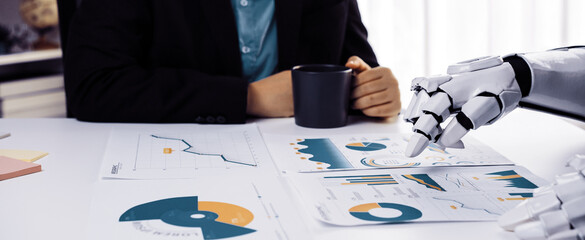 A business professional engages with robotic technology, analyzing financial reports while enjoying...