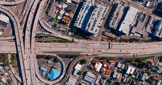 Hectic traffic on the interchange and highways of the metropolis. Multiple cars are parked in the streets on the rooftop parking lots. Los Angeles, California, USA. Top view.
