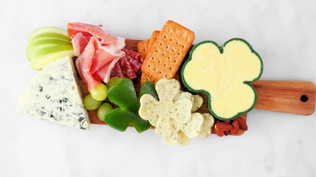 St Patricks Day theme charcuterie board against a white marble background. Slow rotating motion. Assortment of cheese, meat, fruit and vegetable appetizers. Top view.