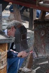 Welder wearing a protective mask, joining metal pieces with an arc welder, creating sparks during boat hull maintenance