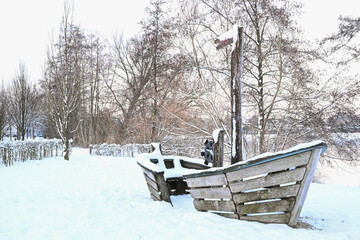 Wooden playground boat covered in deep snow in a winter park near Zaltbommel. Nostalgic winter scene of a deserted playground in the Netherlands. Concept of seasonal silence.