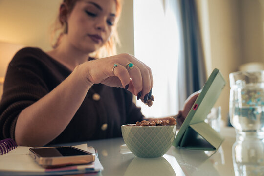 Woman working from home while choosing healthy snack and using tablet