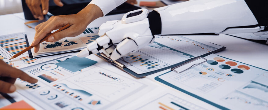 A robotic arm engages with data analysis on printed reports, showcasing a blend of human and machine collaboration in a vibrant office setting.Noogenesis
